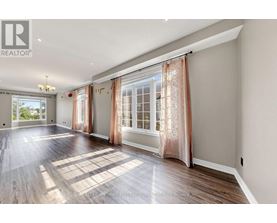 A spacious room with wooden floors and large windows with curtains.