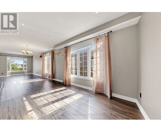 A spacious room with wooden floors and large windows with curtains.