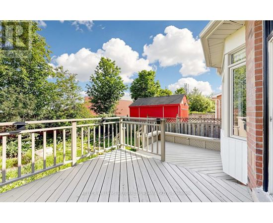 A wooden deck with a railing and a red building in the background.