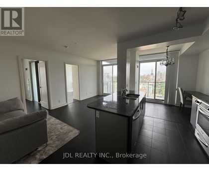 A spacious kitchen and living room with a grey sofa and a chandelier.
