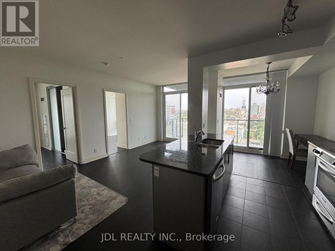 A spacious kitchen and living room with a grey sofa and a chandelier.