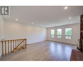 A spacious room with wooden flooring and a window with a view of trees.
