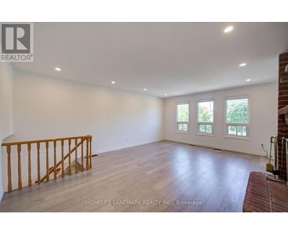 A spacious room with wooden flooring and a window with a view of trees.