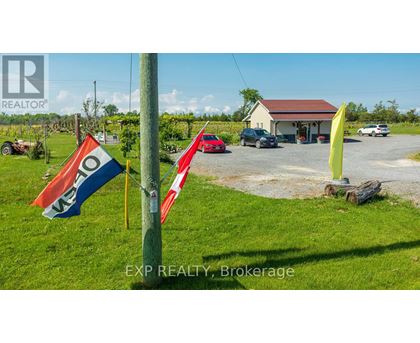 A real estate sign is displayed in a grassy field with a house and cars in the background.