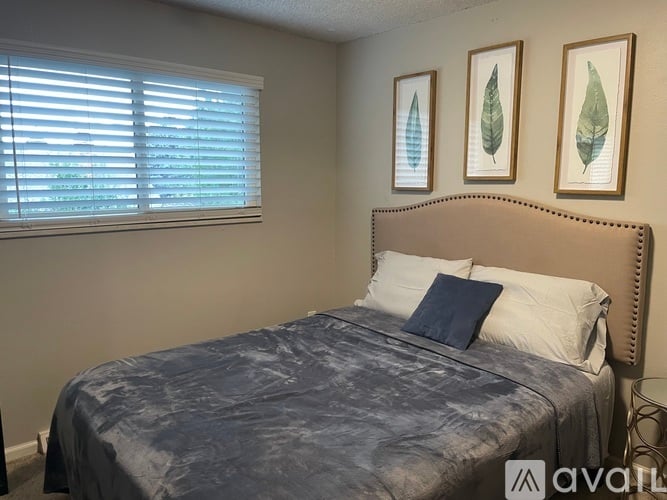 A bedroom with a bed, two pillows, and two framed leaves on the wall.