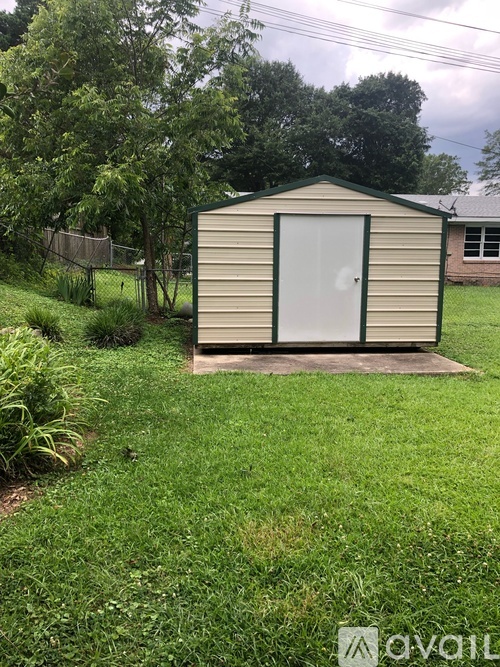 A shed with a white door is surrounded by a grassy area and trees.