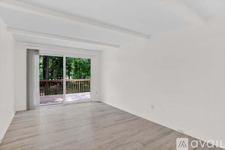 A spacious room with wooden flooring and a sliding glass door leading to a deck.
