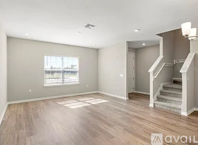 A spacious room with wooden flooring and a staircase leading to another room.