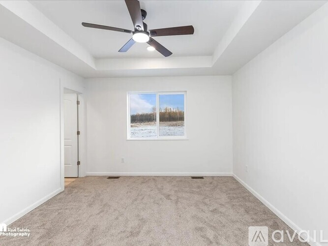 A room with a ceiling fan and a window showing a view of trees.