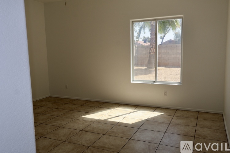 A room with a window showing a view of a fence and trees outside.