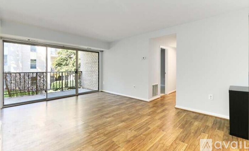 A spacious room with wooden flooring and a sliding glass door leading to a balcony.