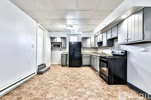 A kitchen with black appliances and brown tile flooring.