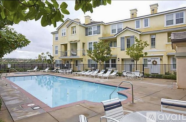 A large swimming pool is surrounded by lounge chairs in front of a two-story apartment building.