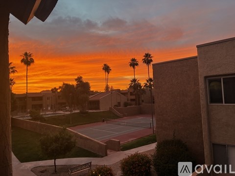 A sunset view from a window overlooking a tennis court and palm trees.