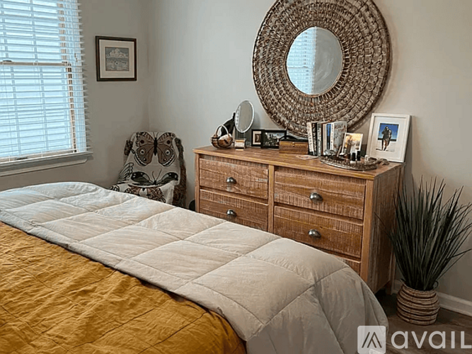 A bedroom with a bed, chair, and dresser with a mirror and picture frame.