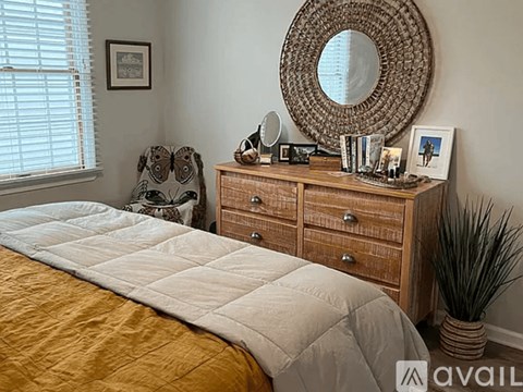 A bedroom with a bed, chair, and dresser with a mirror and picture frame.