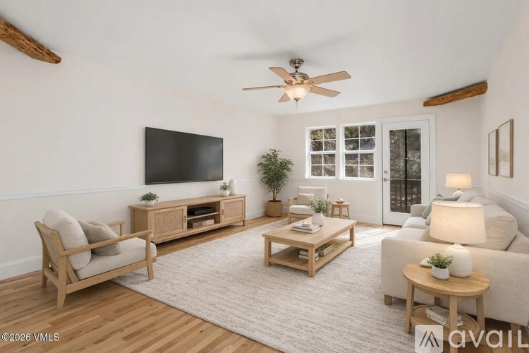 A living room with a flat screen TV, a wooden entertainment center, a sofa, a chair, a coffee table, and a ceiling fan.