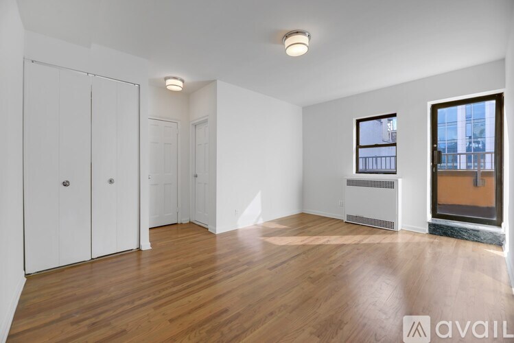 A room with wooden floors and white walls, with a window showing a city view.