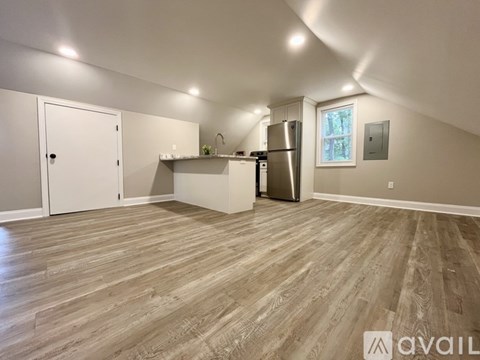 A spacious room with wooden flooring and a kitchen area with a refrigerator and sink.