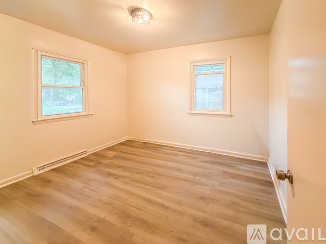 A room with wooden flooring and two windows.