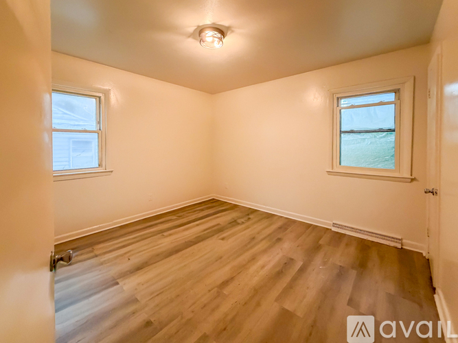 A room with wooden flooring and two windows.