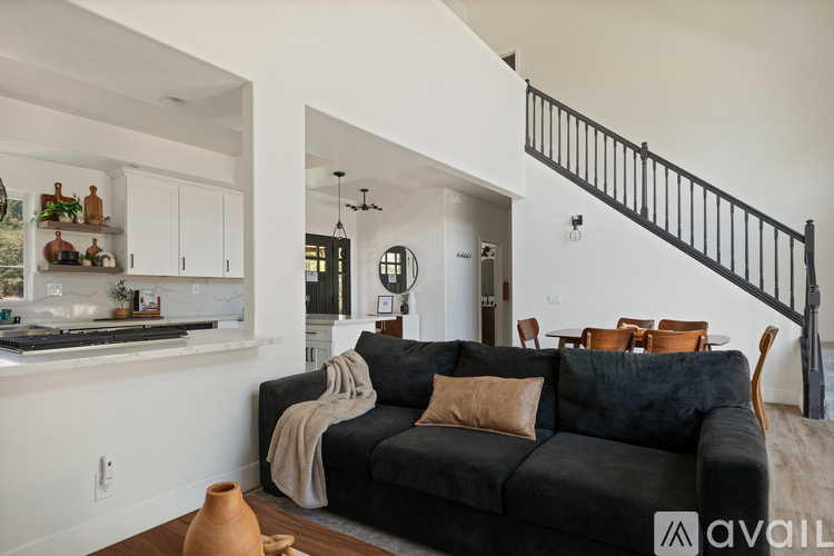 A black couch with a tan throw blanket sits in a living room with a staircase in the background.