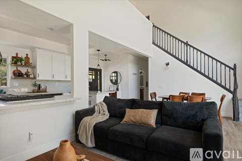 A black couch with a tan throw blanket sits in a living room with a staircase in the background.