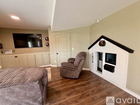 A living room with a grey couch, a brown chair, and a television mounted on the wall.