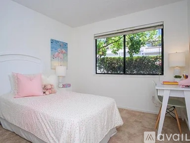 A bedroom with a white bed and a window with a view of trees.