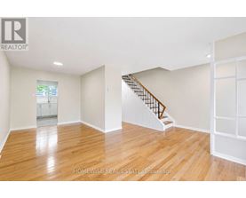 A spacious room with wooden flooring and a staircase.