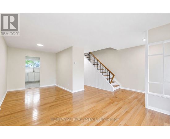 A spacious room with wooden flooring and a staircase.