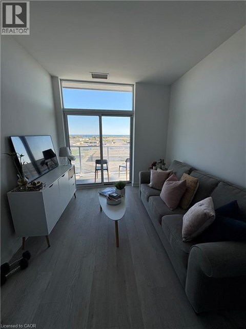 A living room with a grey couch and a large window overlooking a parking lot.