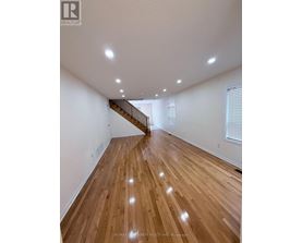 A spacious room with wooden flooring and a staircase.