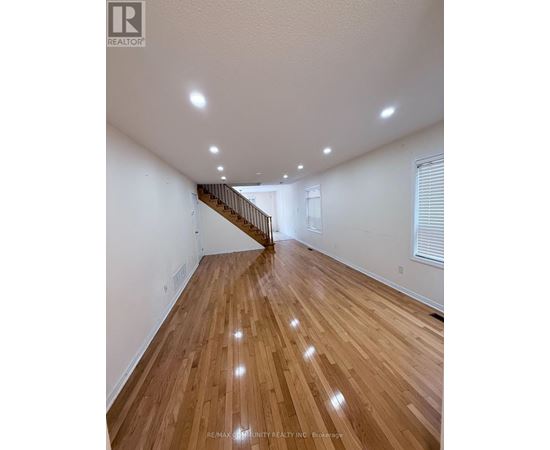 A spacious room with wooden flooring and a staircase.