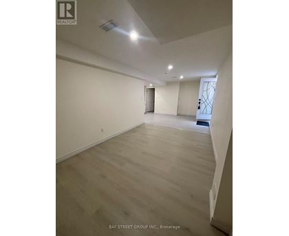 A spacious room with wooden flooring and white walls, with a door on the right side.