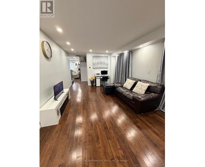 A living room with a brown leather couch and wooden floors.