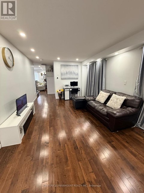 A living room with a brown leather couch and wooden floors.
