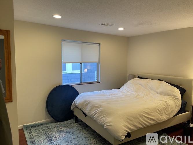 A bedroom with a bed, a round pillow, and a window with blinds.
