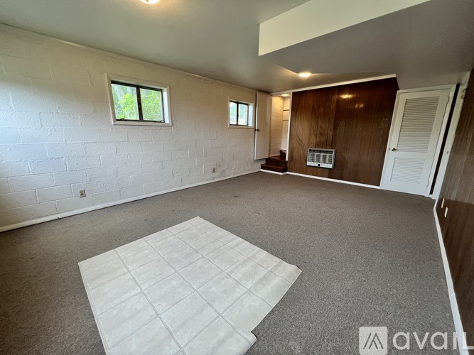 A spacious room with a white mattress on the floor and two windows.