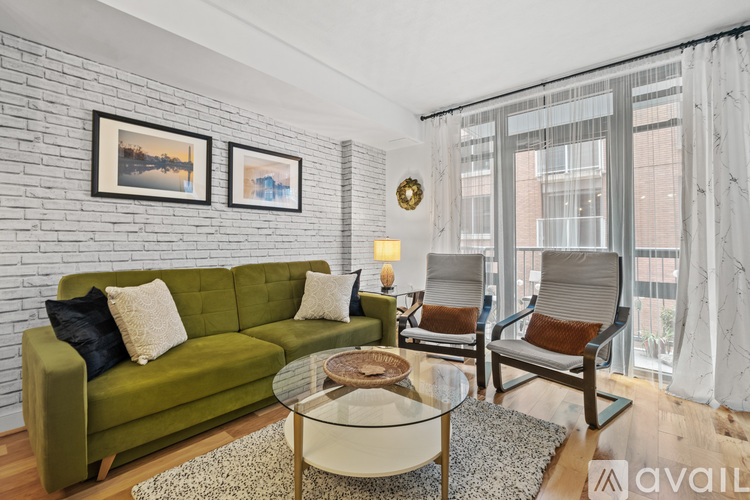 A living room with a green couch, a glass table, and a white brick wall.