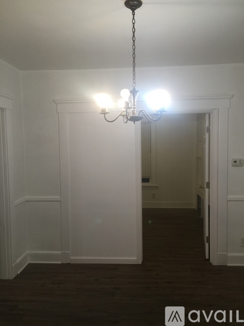 A chandelier hangs from the ceiling in a room with white walls and dark wood flooring.