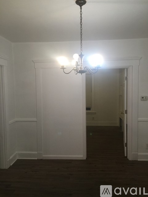 A chandelier hangs from the ceiling in a room with white walls and dark wood flooring.