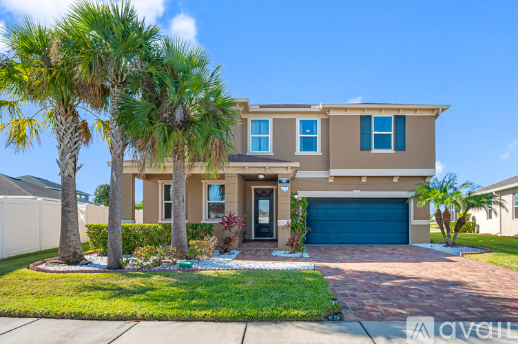 A house with a blue garage door is surrounded by palm trees.