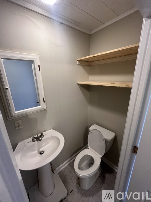 A bathroom with a toilet, sink, mirror and shelves.