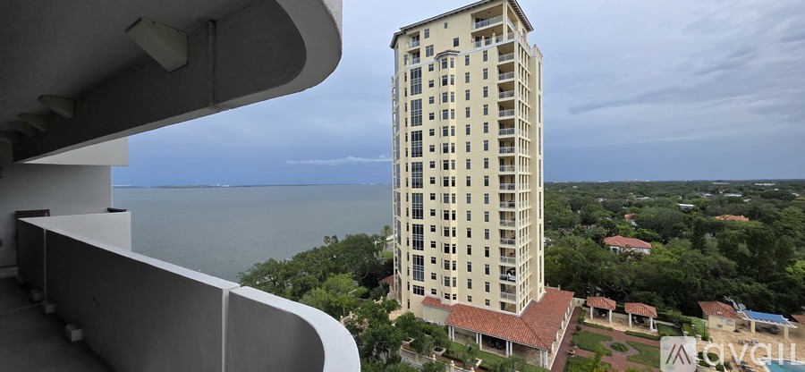 A tall building with a balcony overlooking a body of water and greenery.