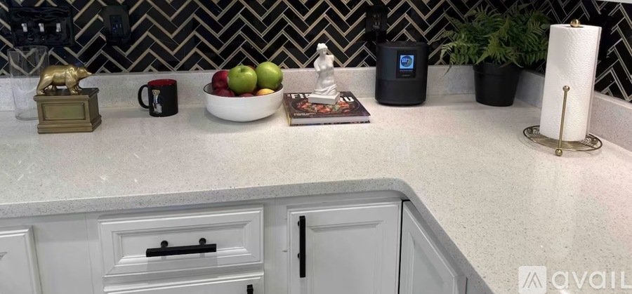 A kitchen counter with a bowl of fruit, a mug, a statue, and a plant.