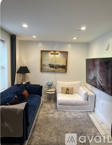 A living room with a blue couch, a white chair, and a painting on the wall.