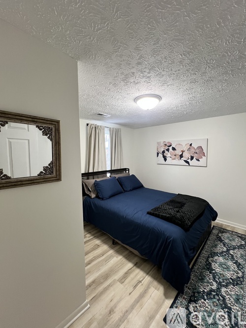 A bedroom with a blue bed and a painting on the wall.
