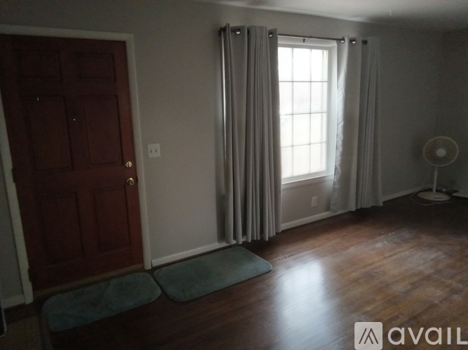 A room with a wooden floor, a red door, a window with curtains, and a fan.