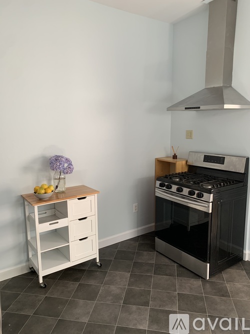 A kitchen with a stove and a cart with fruit on it.